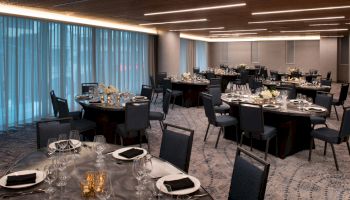 The image shows an elegant banquet hall set up with round tables and chairs, each table adorned with dining ware and floral centerpieces.