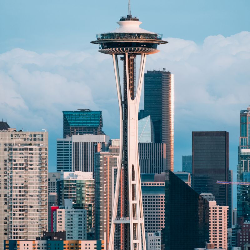 The image showcases the Space Needle, an iconic observation tower, against the skyline of Seattle with modern skyscrapers in the background.
