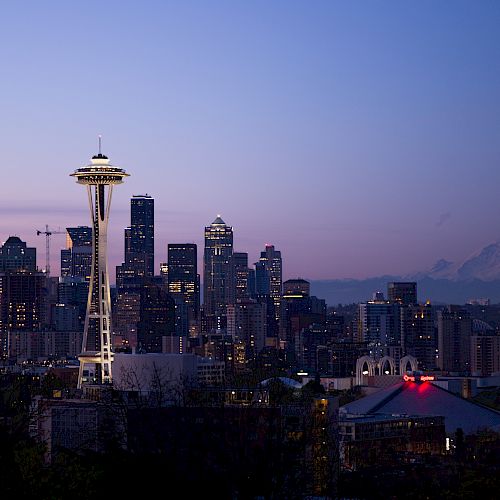 The image shows a city skyline at dusk with a distinctive tower, high-rise buildings, and a mountain in the background.
