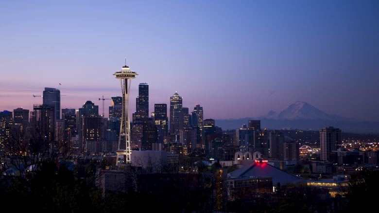 This image shows a city skyline at dusk with a prominent tower, numerous buildings, and a mountain in the background, all under a twilight sky.