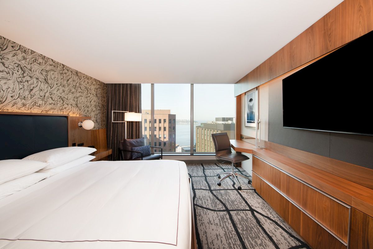 A modern hotel room features a large bed, flat-screen TV, desk, and floor-to-ceiling window with a city view, finished the sentence.