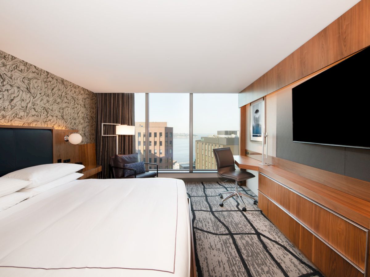 A modern hotel room features a large bed, flat-screen TV, desk, and floor-to-ceiling window with a city view, finished the sentence.